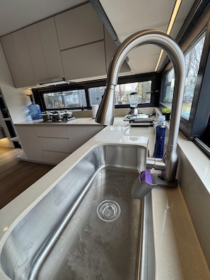 A modern kitchen with a stainless steel sink, a window with a view, and a countertop with various kitchen items.