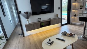 Moderni olohuone, jossa on litteänäyttöinen televisio, sohvapöytä ja kirjahylly.