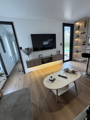 A modern living room with a flat-screen TV, a coffee table, and a bookshelf.