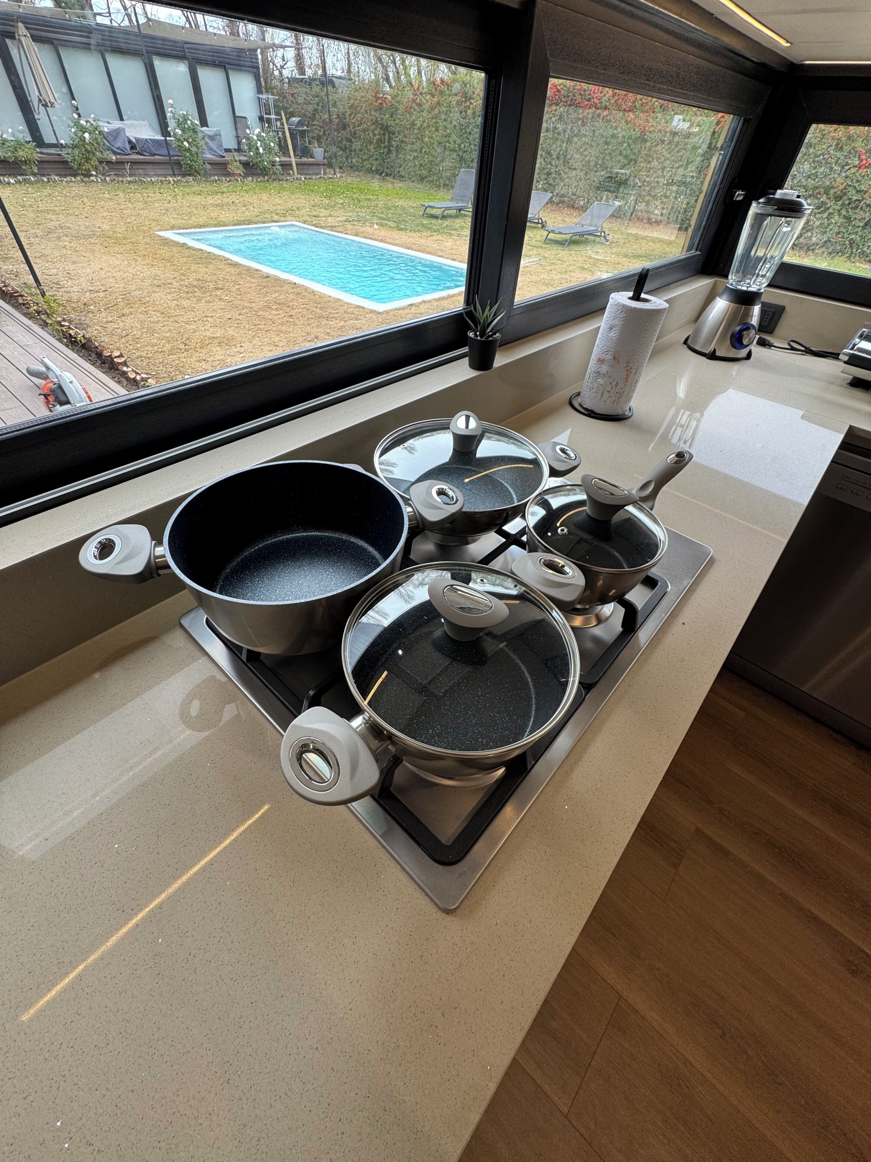 Une cuisine équipée d’une cuisinière à gaz, de casseroles, d’un mixeur et offrant une vue sur une cour arrière avec une piscine.