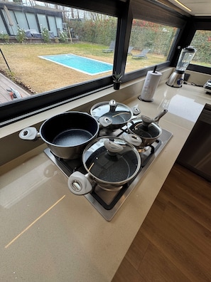 A kitchen with a gas stove, pots, a blender, and a view of a backyard with a pool.
