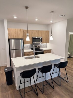 A modern kitchen with a central island, stainless steel appliances, pendant lighting, and a clean, minimalist design. - Cozy 1-bedroom apartment by Piedmont park (Atlanta)