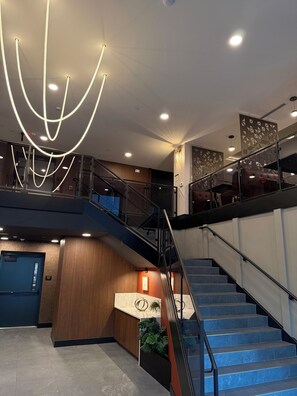 Een moderne hotel lobby met een trap, een receptiebalie en een decoratieve lamp.
