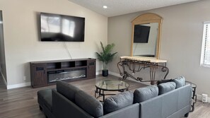 A living room with a flat-screen TV, a large mirror, a sofa, a coffee table, and a plant.