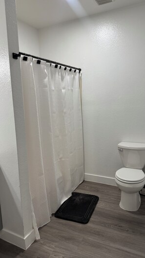 Un baño con cortina de ducha, un inodoro y un tapete negro en el suelo.