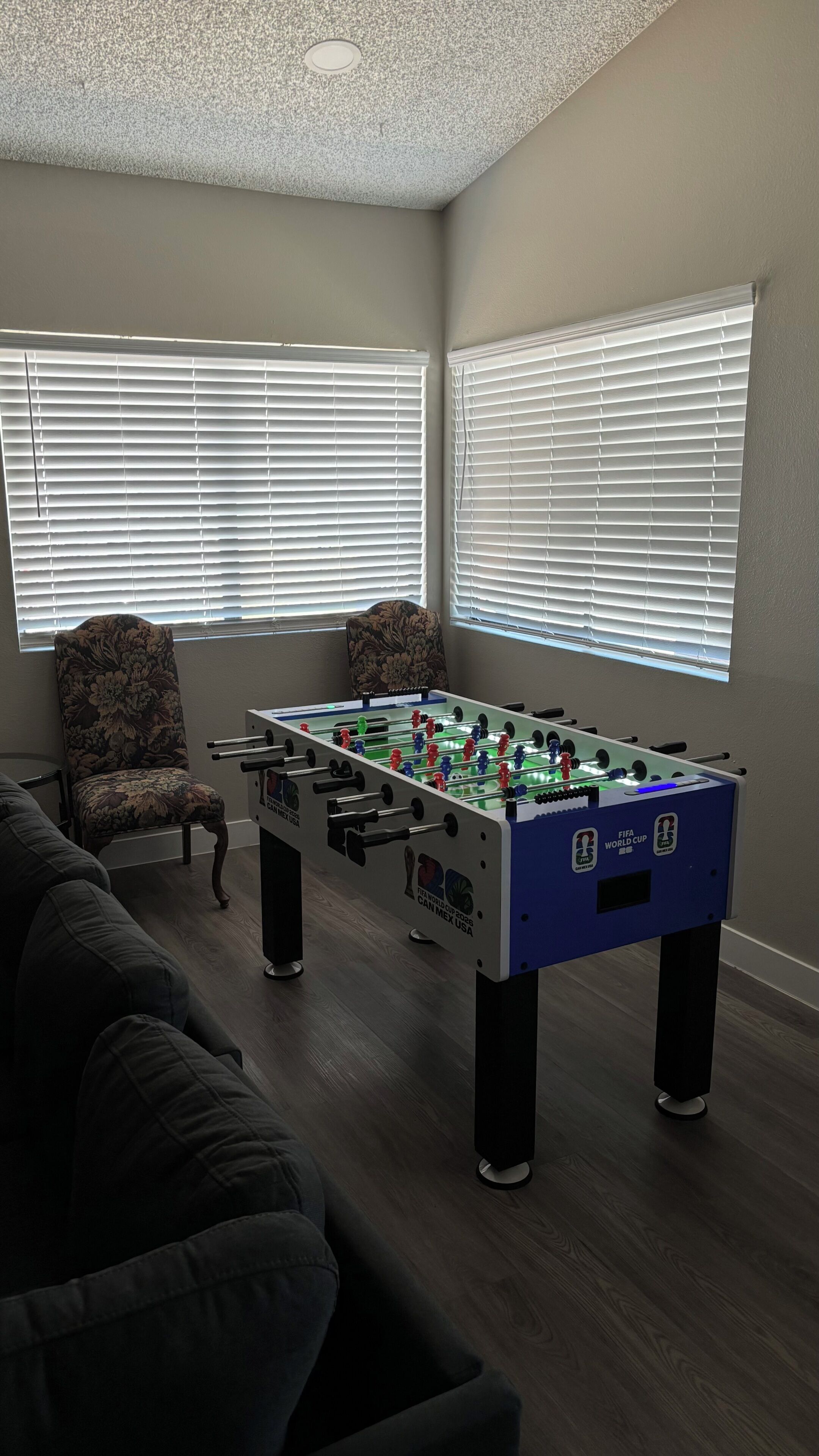 Una habitación con mesa de fútbol de mesa, una butaca estampada y un sofá.