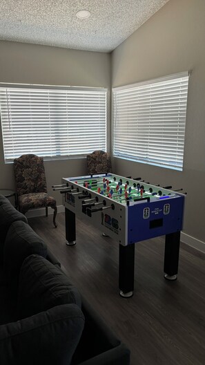 Una habitación con mesa de fútbol de mesa, una butaca estampada y un sofá.