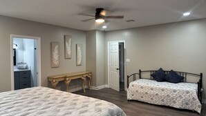 Quarto com duas camas, um ventilador de teto, cômoda e uma porta que dá para outro espaço.