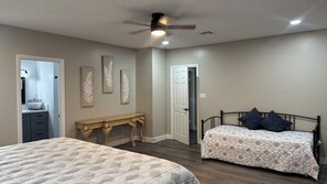 Un dormitorio con dos camas, un ventilador de techo, un aparador y una puerta que da a otra habitación.