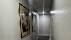 Um corredor com quadros nas paredes, piso de madeira e iluminação no teto.