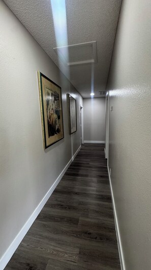 A hallway with framed artwork on the walls, a wooden floor, and a ceiling light.
