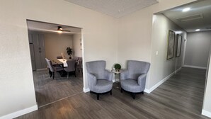 Um interior moderno com área de refeições, duas poltronas, uma mesinha com uma planta e um ventilador de teto.