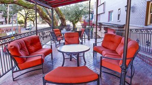 Un balcon avec des chaises à coussins rouges et une table ronde, donnant sur une rue où circule un tramway.