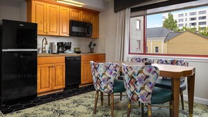 Une cuisine compacte avec des meubles en bois, un réfrigérateur noir et un coin repas doté de chaises à motifs.