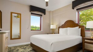 Une chambre d’hôtel avec un grand lit, une table de chevet avec une lampe, une commode, une fenêtre avec vue et un ventilateur de plafond.