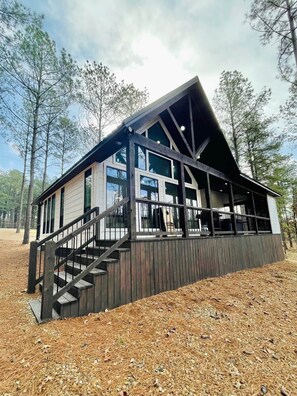 A cabin with a wooden deck, large windows, and a staircase leading to the entrance. - Little Darlin! Romantic Couples Cabin!!! Pet Friendly! (Hochatown)