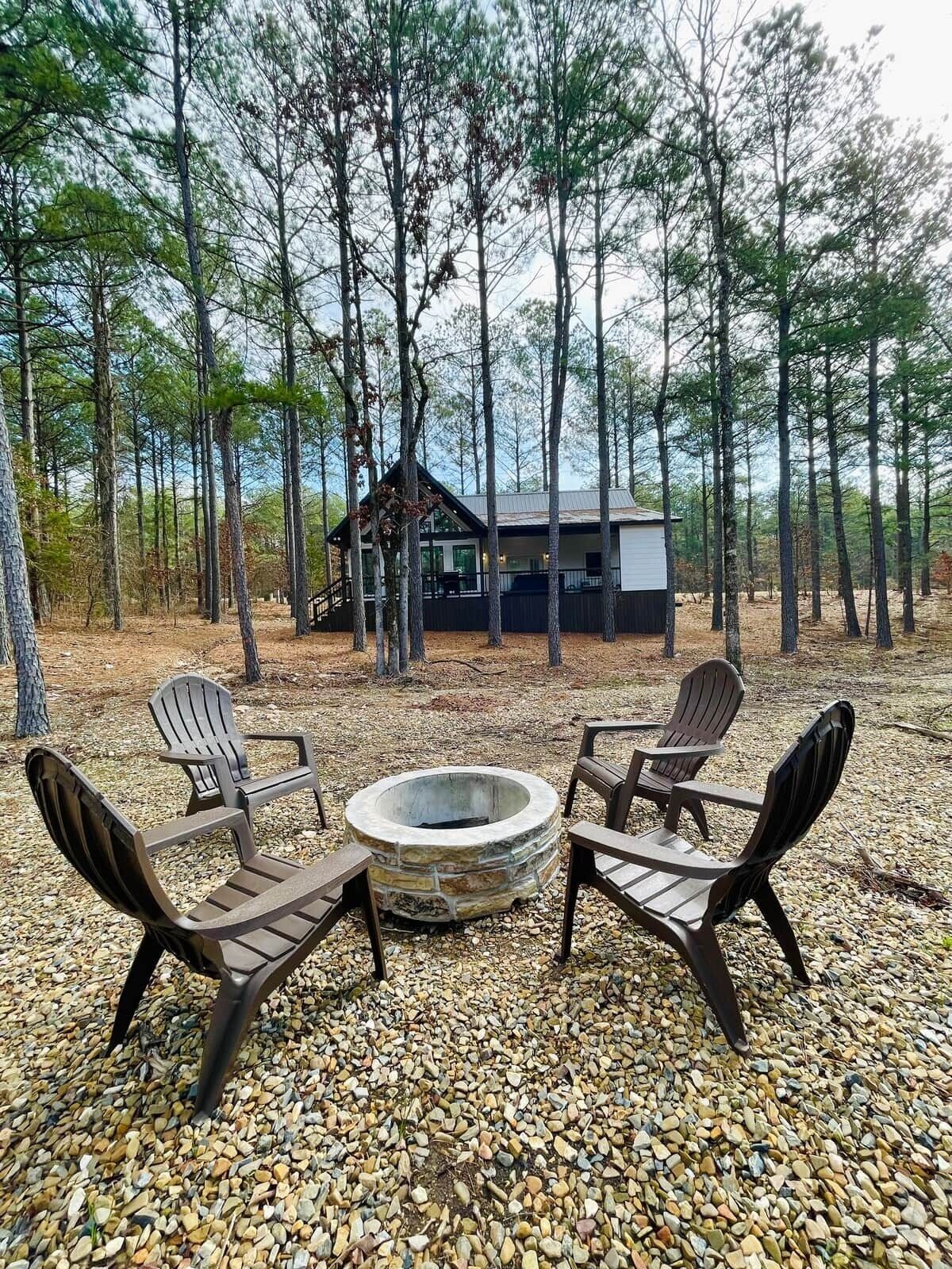 Una cabaña con un hogar de piedra y sillas Adirondack en un entorno boscoso.
