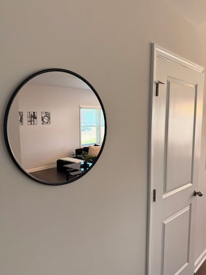 A round mirror on a wall, a white door, and a window with blinds.