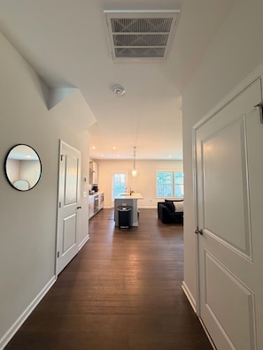 A hallway with a kitchen area, a dining table, and a black couch.