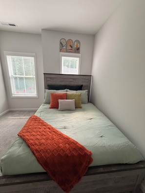 A bedroom with a bed, a window, and a wall-mounted artwork.
