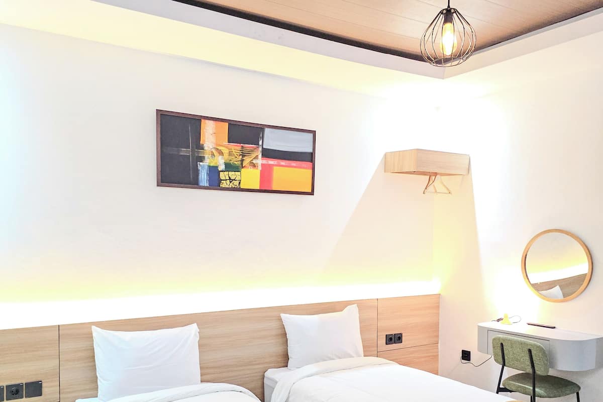Habitació d'hotel amb dos llits, un escriptori, una cadira, una làmpada, un mirall i un quadre a la paret.