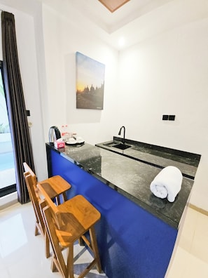 A compact kitchen with a blue countertop, a sink, a kettle, and a painting on the wall. - Lodji Svarga Premiere Villa (Sleman)