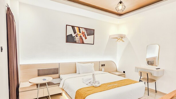 A modern hotel room with a bed, bedside table, chair, and a painting on the wall.
