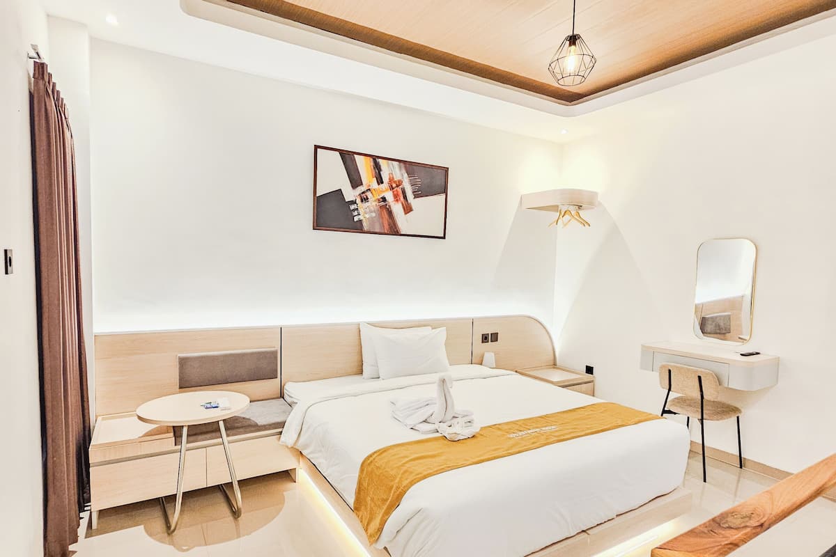 Habitació d'hotel moderna amb llit, taula de nit, cadira i un quadre a la paret.