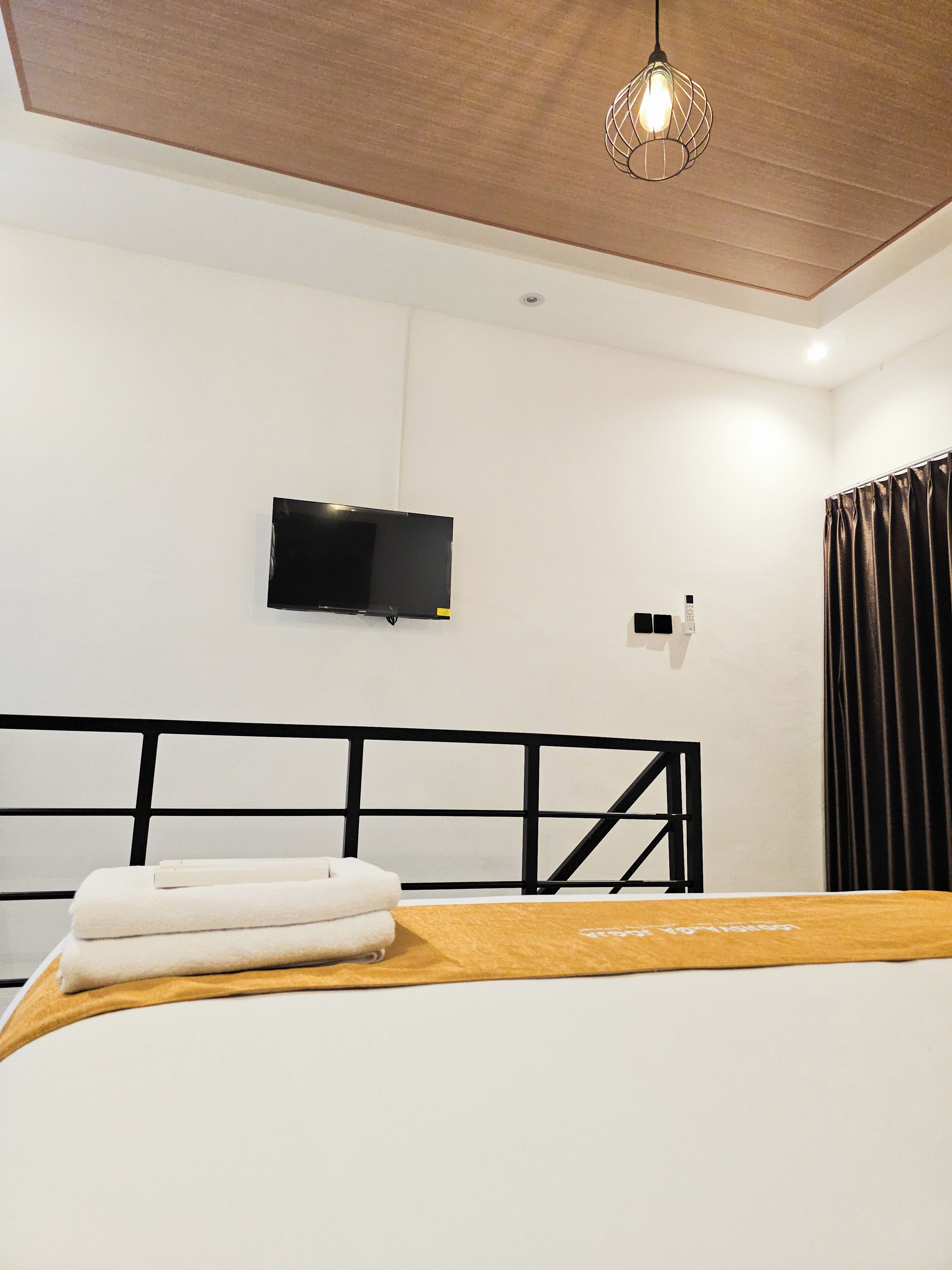 A bedroom with a bed, a television mounted on the wall, a ceiling light fixture, and a window with curtains.
