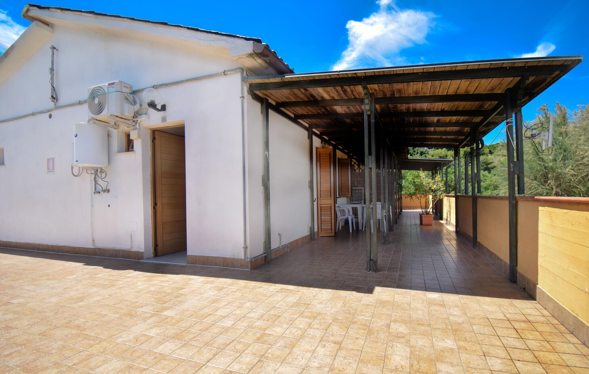 A covered outdoor area with a tiled floor, a table with chairs, and a building with an air conditioning unit.