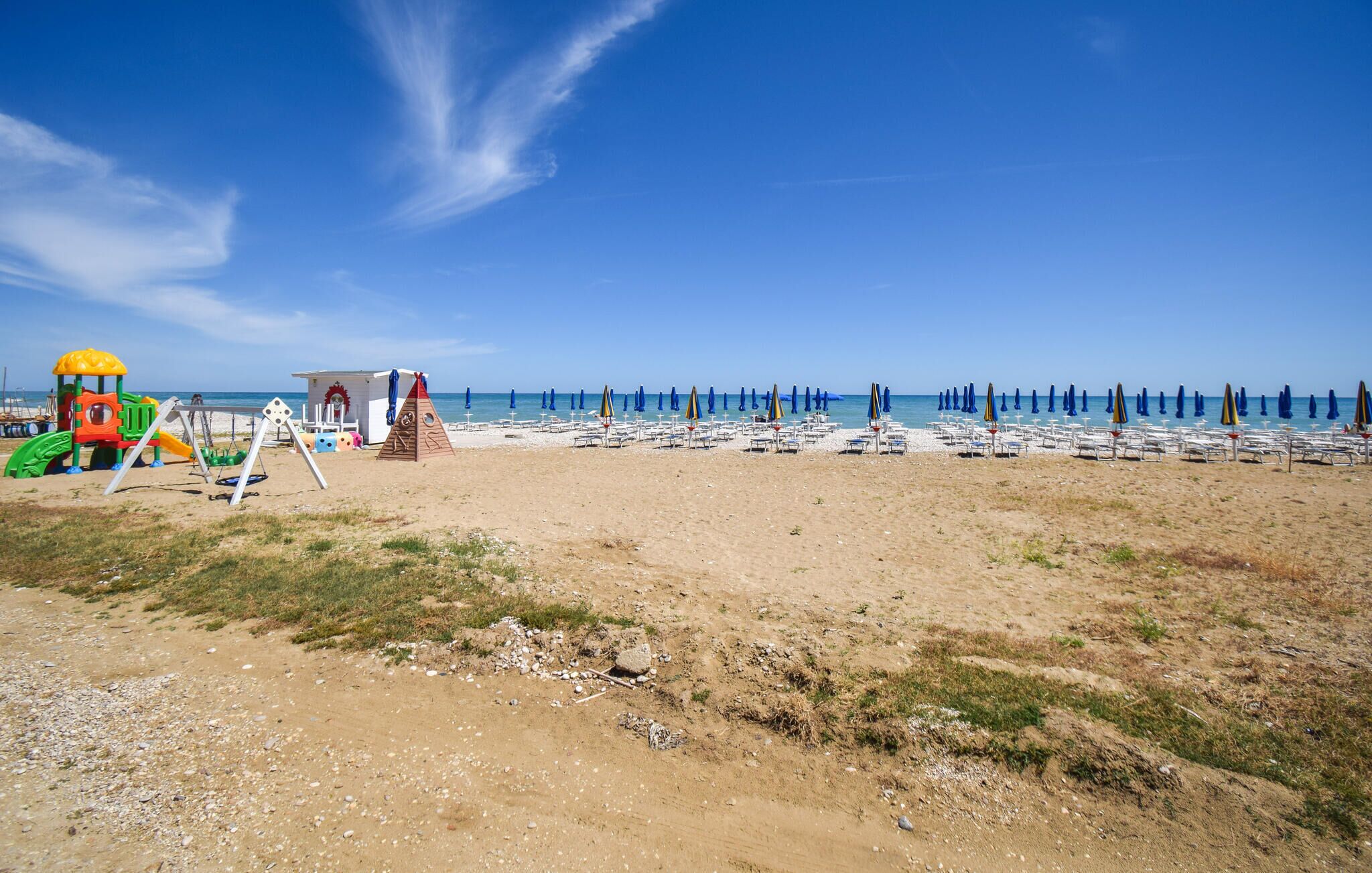Une plage dotée d’une aire de jeux pour enfants, de parasols et de chaises longues.