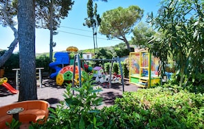 Ein Spielplatz mit verschiedenen Spielgeräten, umgeben von Grünflächen und Bäumen.