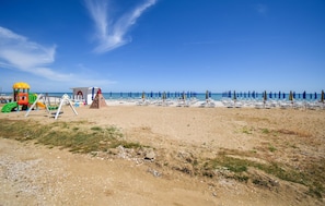 Ein Strand mit Kinderspielplatz, Strandliegen und Sonnenschirmen.