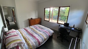 Un dormitorio con cama, escritorio y silla, armario y ventana con vistas a la vegetación.