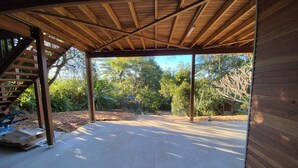 Un garaje abierto con techo de madera, suelo de concreto y una escalera que conduce a una zona cubierta.