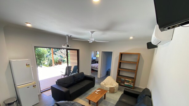 Una sala de estar moderna con un sofá, un sillón tipo puff, una mesa de centro, un televisor y un ventilador de techo.