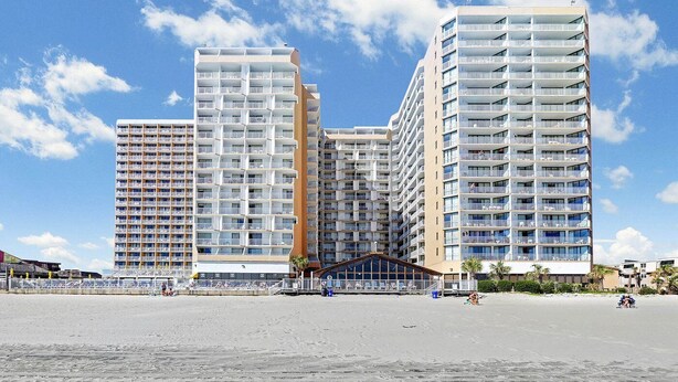 Un hotel de gran altura con múltiples balcones, vista al mar y una entrada principal.