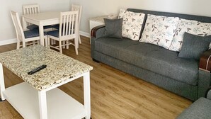 Un salón con una mesa blanca, un sofá gris y un cuadro de una playa.