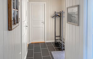 Ein Flur mit einer weißen Tür, einem Kleiderständer mit Kleidung, einem gerahmten Bild an der Wand und einem gefliesten Boden.