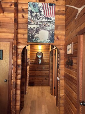 Ein Holzblockhaus-Interieur mit einem Flur, der zu einer Tür führt, einer aufgehängten amerikanischen Flagge und rustikaler Wanddekoration.