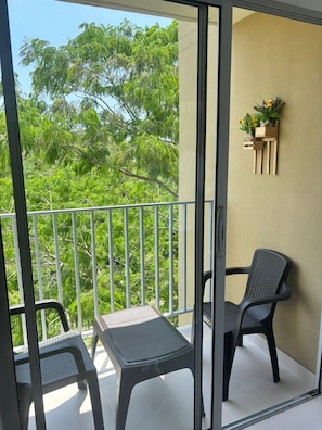 A balcony with a table and two chairs, a wooden planter with flowers, and a view of green trees. - Crislaye House (Santa Marta)