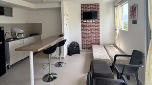 Ett kompakt kök med en matplats, en tv som är monterad på en tegelvägg och ett fönster med gardiner.