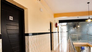 Pasillo de hotel con una puerta negra marcada '102', un extintor y una escalera que lleva a un nivel superior.