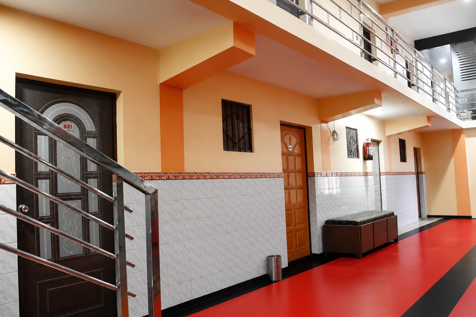 Un pasillo de hotel con alfombra roja, una escalera con barandillas metálicas y una puerta de madera.