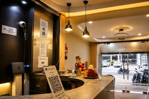 Ein Hotel-Rezeptionsbereich mit einer Theke, einem Schild für Videoüberwachung, einem Google Pay-Logo und einem QR-Code für SHIMLUP.