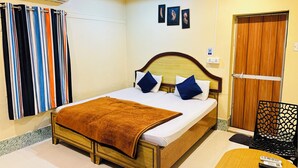 Habitación de hotel con una cama, cabecera de madera, manta marrón, aire acondicionado de pared, ventana con persianas y puerta con panel de madera.