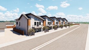 Una hilera de casas modernas de dos pisos, con balcones, un camino de entrada pavimentado y cielo despejado.
