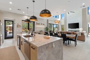 A modern kitchen with a central island, dining area with chairs, a sofa, and a TV mounted on the wall. - Luma Ridge - `26 Luxury Build, Pool & Spa, Views (Sedona)