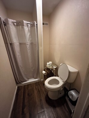 Een kleine badkamer met douchegordijn, toilet en prullenbak.