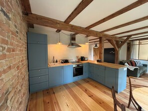 A kitchen with blue cabinets, wooden beams, a wooden countertop, and a dining area with a table and chairs.